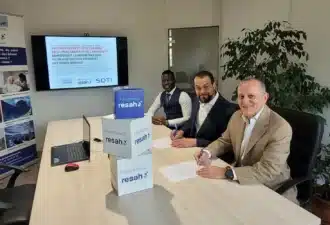 Signature de partenariat entre SOTI et Groupe PRISME pour optimiser la gestion des parcs mobiles, avec trois hommes signant des documents dans une salle de réunion.