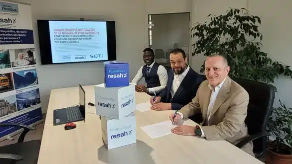Signature de partenariat entre SOTI et Groupe PRISME pour optimiser la gestion des parcs mobiles, avec trois hommes signant des documents dans une salle de réunion.