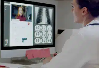Professionnelle de santé en consultation de téléradiologie, analysant des radiographies thoraciques et des scanners sur un ordinateur lors d'une vidéoconférence.